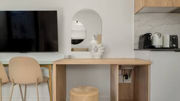 A modern kitchen with a wooden table, two chairs, a round mirror, and a TV mounted on the wall.