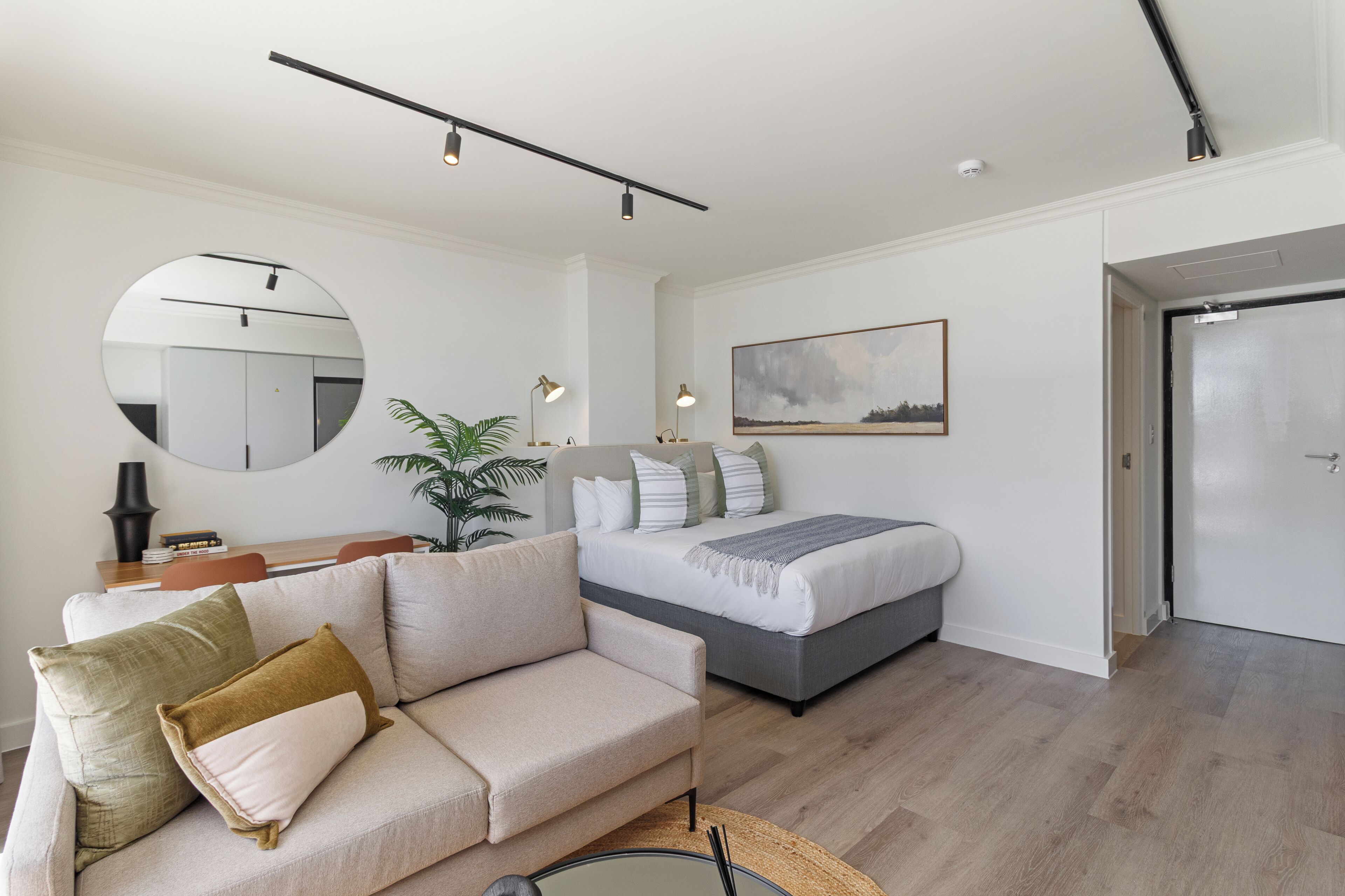 A modern bedroom with a bed, a sofa, a round mirror, and a dining area with a table and chairs.