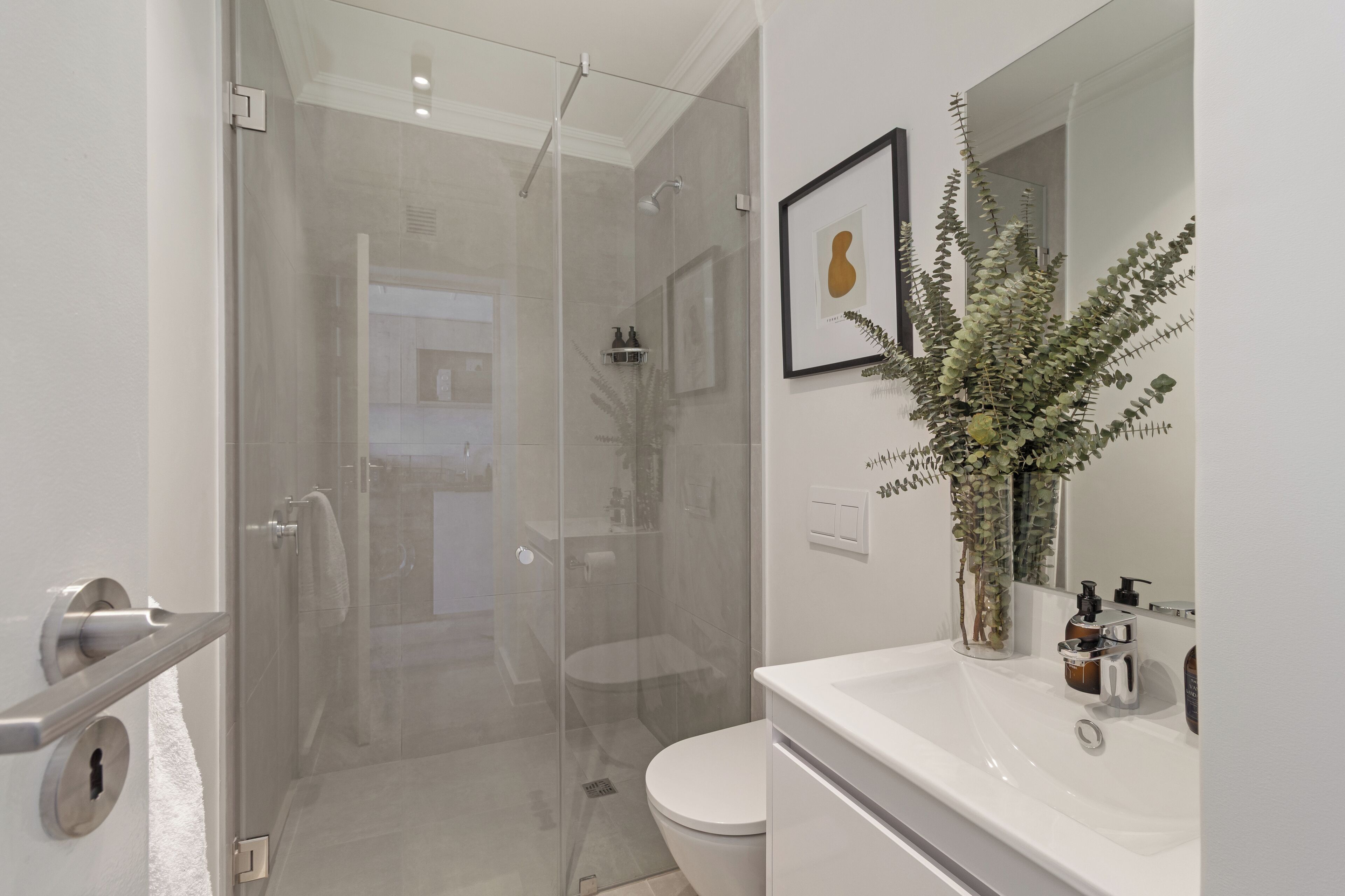 Une salle de bain moderne avec une douche à parois de verre, des toilettes blanches et un lavabo avec un miroir.