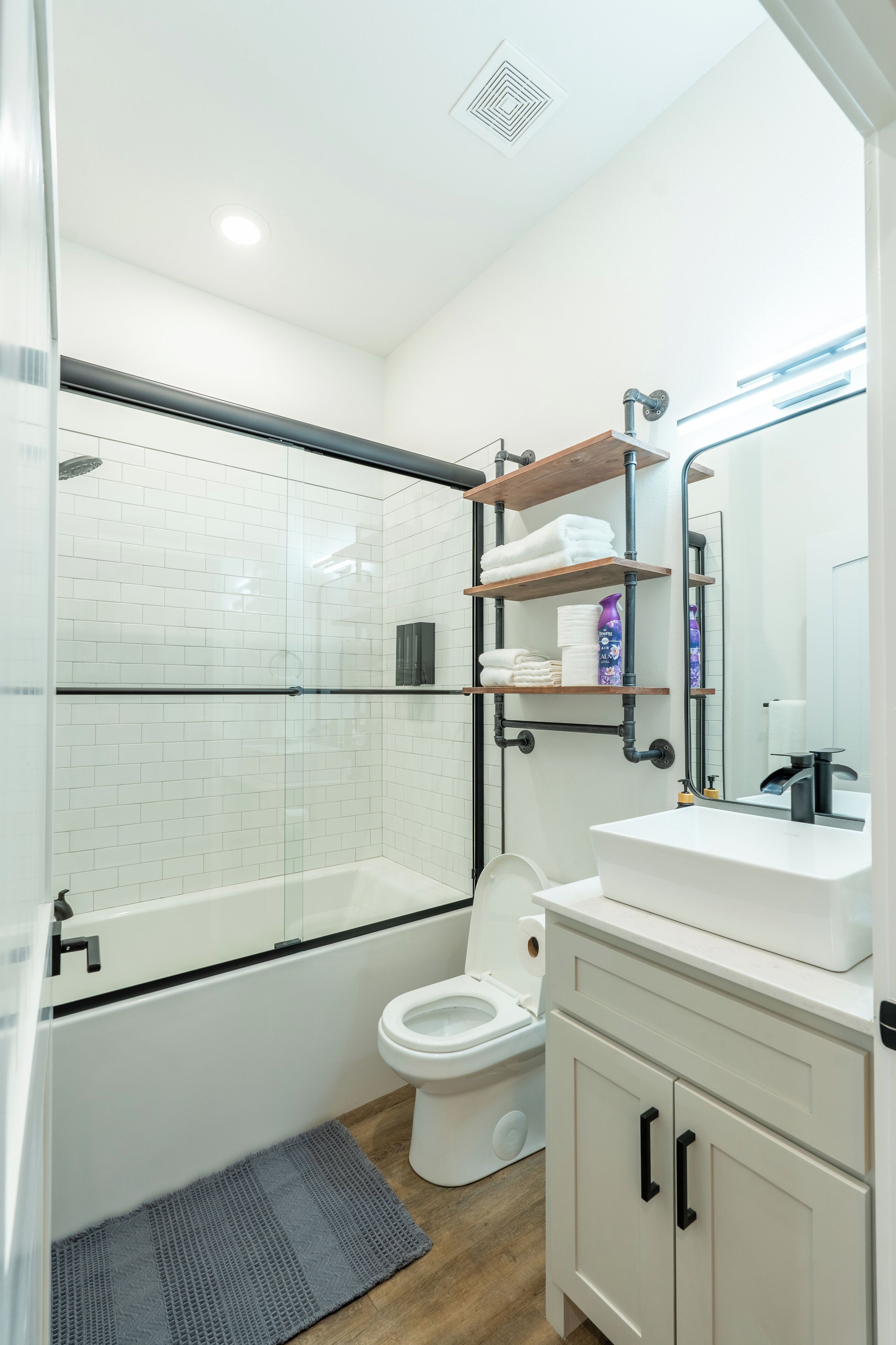 Un baño moderno con ducha de vidrio, inodoro blanco, lavabo blanco y espejo sobre el lavabo.