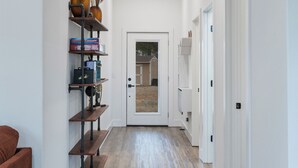 Un couloir doté d’un plancher en bois, de murs blancs et d’une porte au fond qui donne sur l’extérieur.