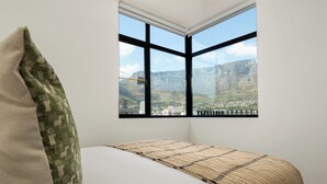 A bedroom with a large window, a bed, and a view of a town and mountains. - The York | Spacious CBD Apartment (Cape Town)