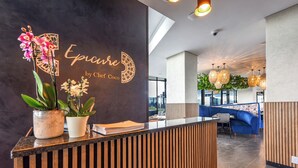 A modern reception area with a dark wall, wooden reception desk, and potted orchids.
