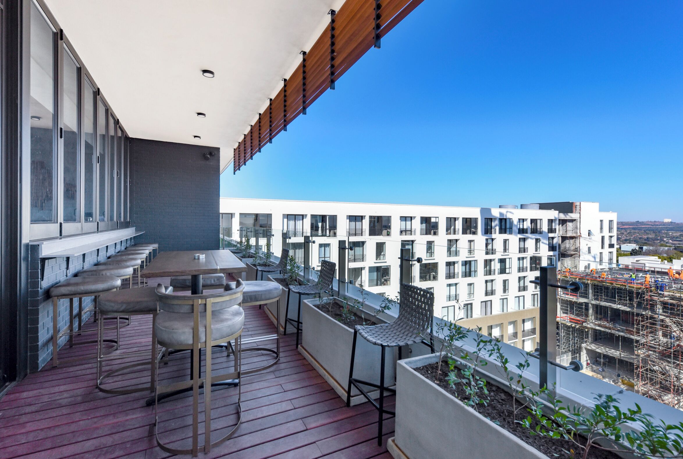 A balcony with a bar area, seating, and potted plants.