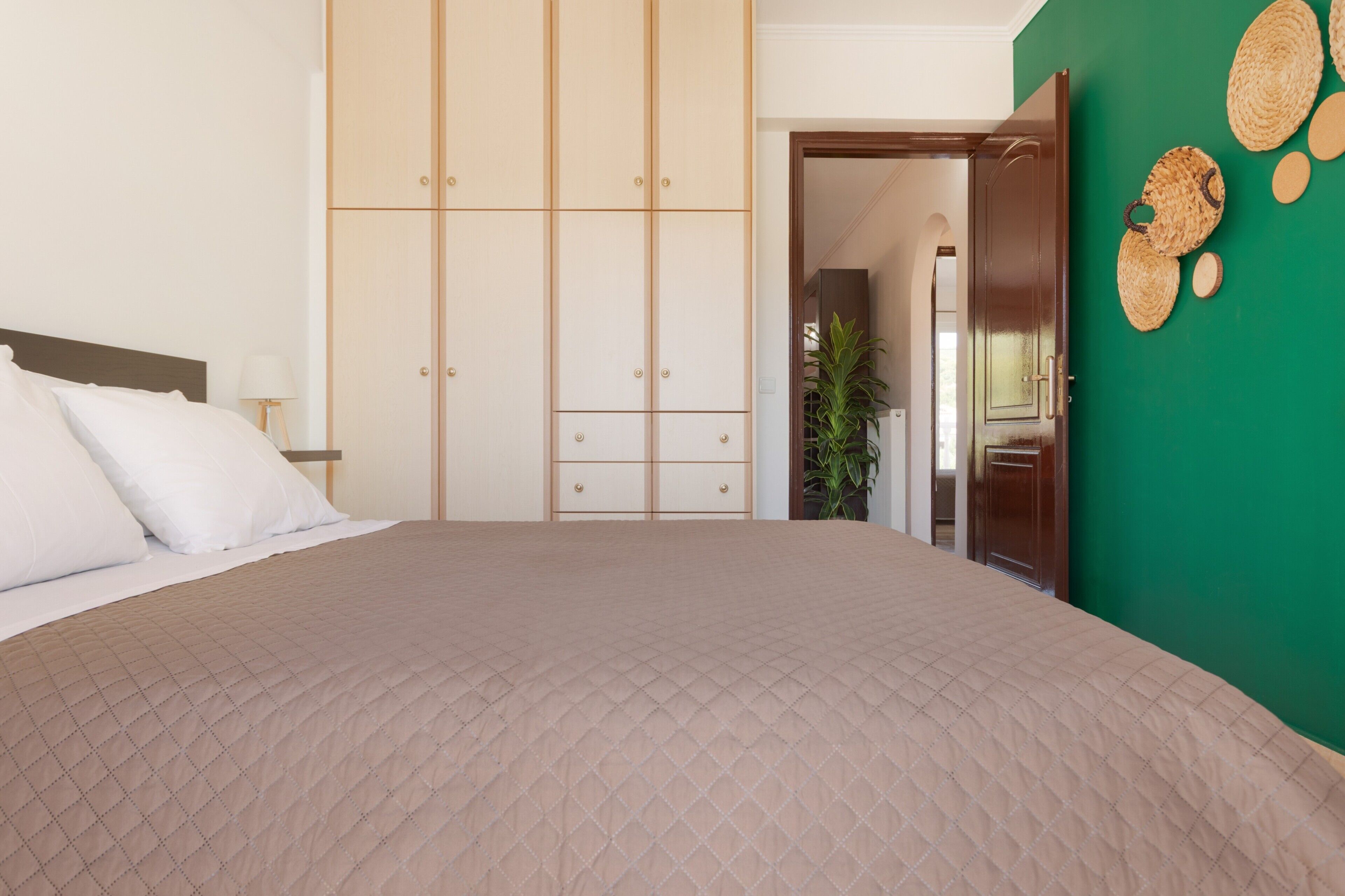 A bedroom with a bed, a wardrobe, a green wall, and a door leading to another room.