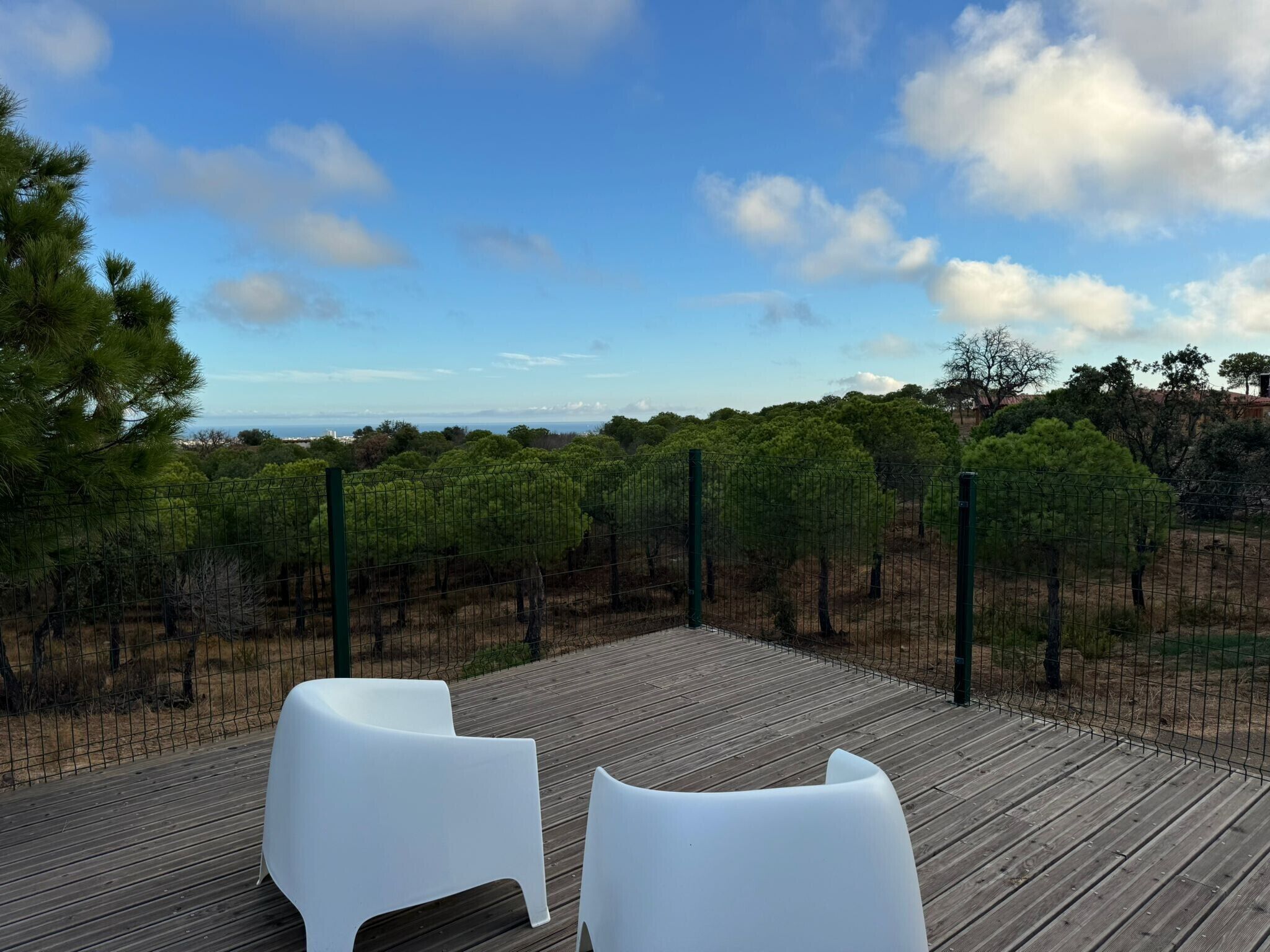 A wooden deck with two white chairs, a vineyard, and a clear sky.