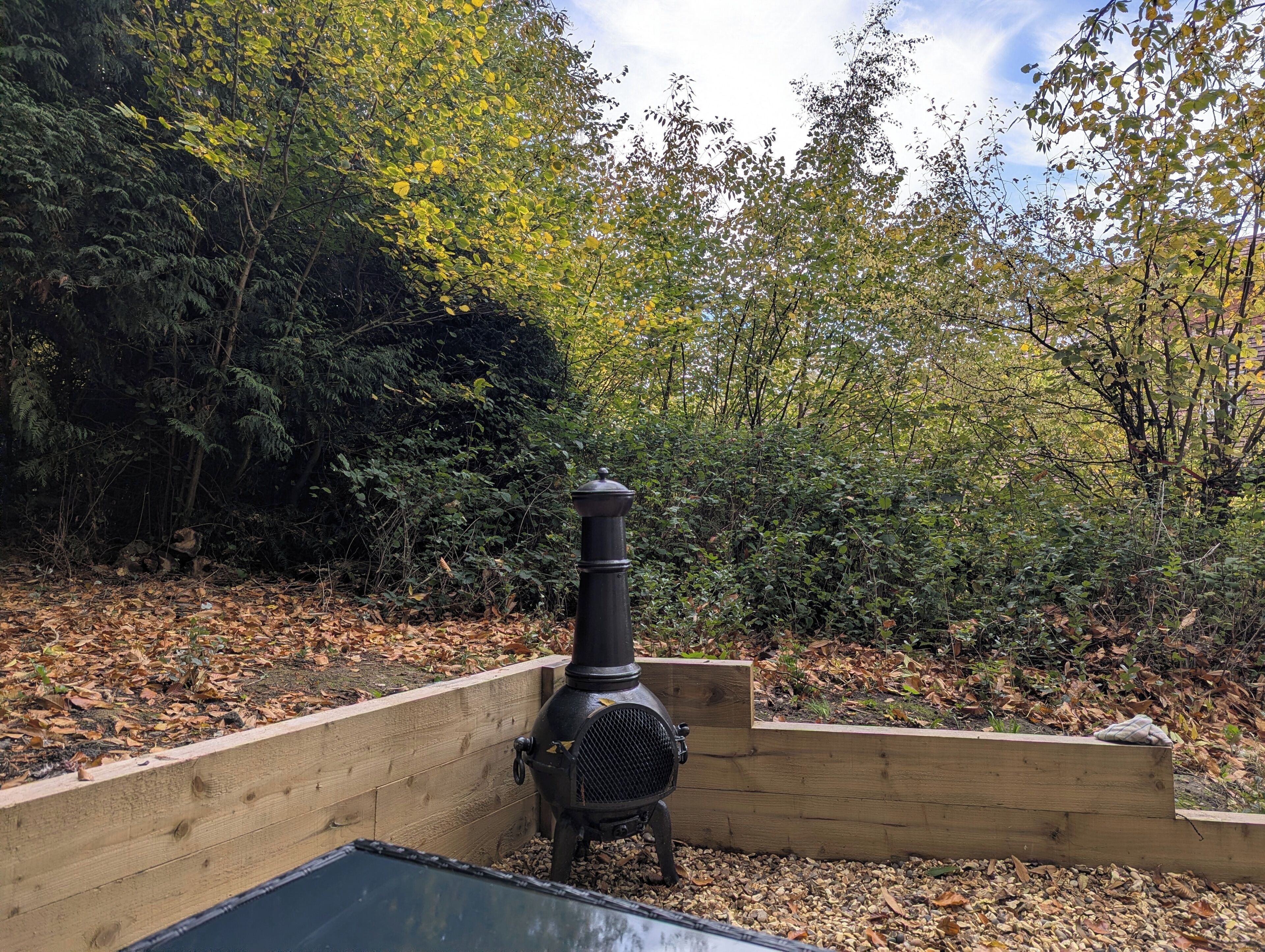 Stufa a legna in un giardino con fioriere di legno e diverse alberature.