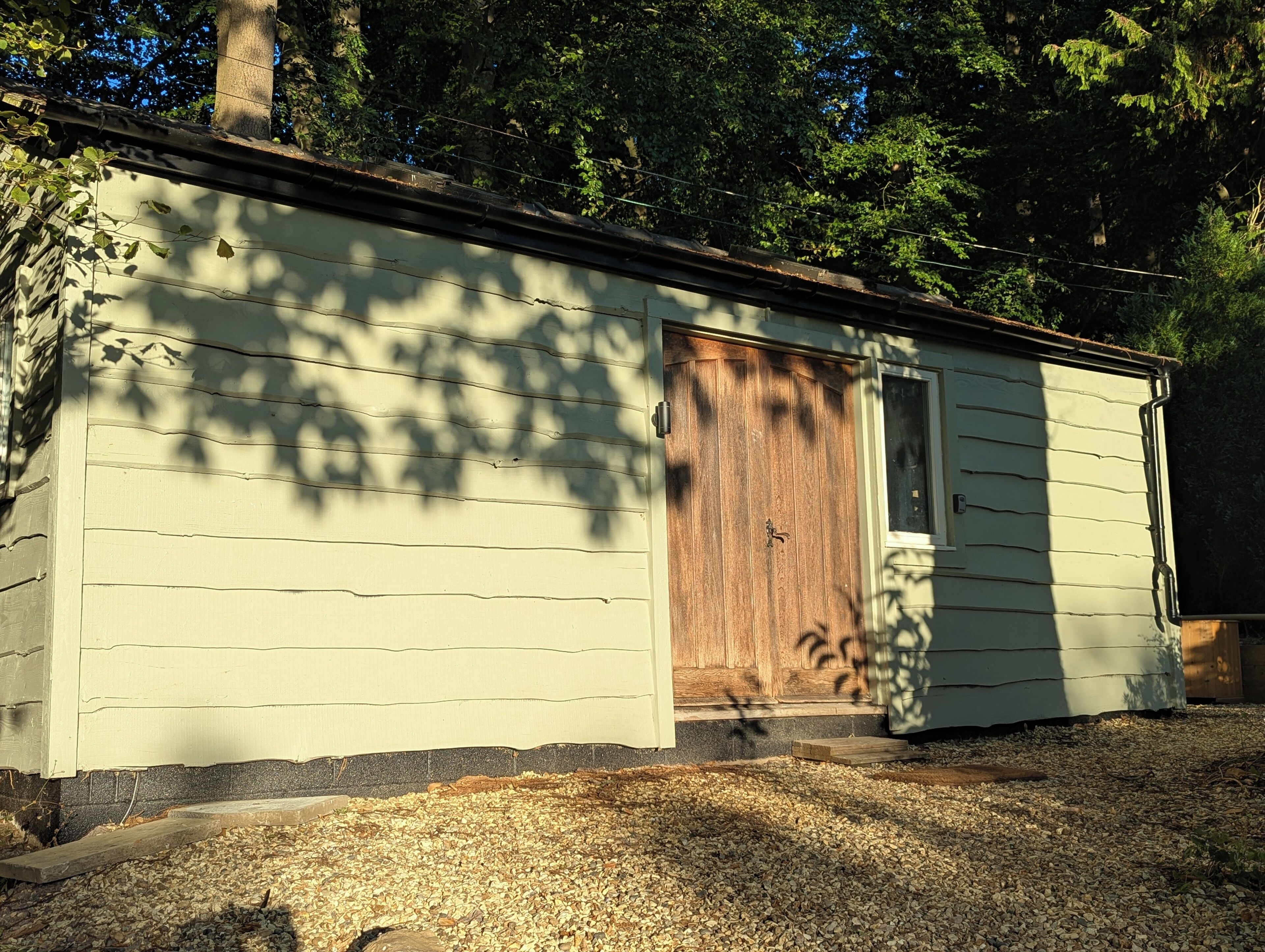A small, single-story building with a wooden door and a window, surrounded by trees.