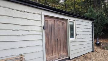 A small wooden shed with a single door and a window, surrounded by gravel and trees.