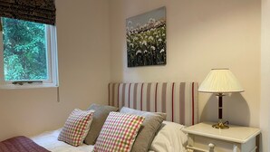 A bedroom with a bed, pillows, a nightstand, a lamp, a window, and a painting on the wall.