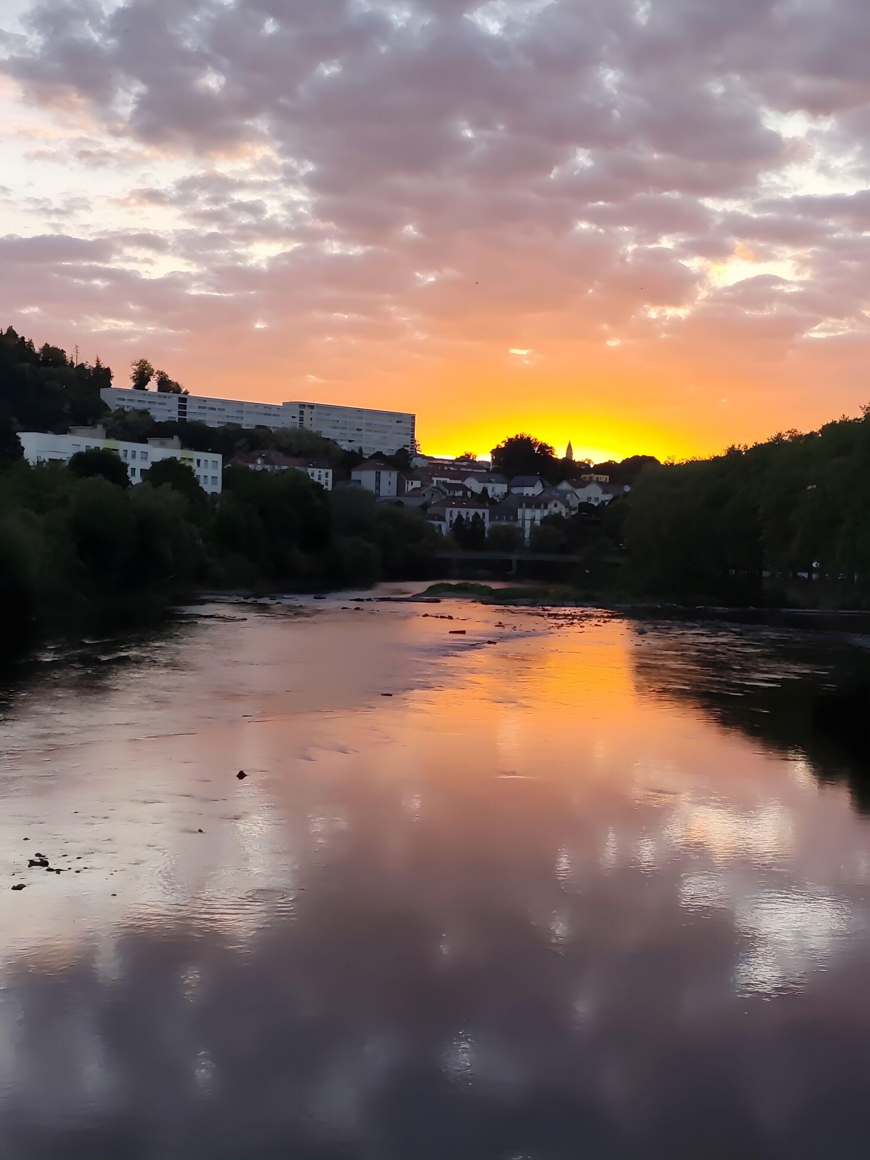 Ein Fluss, der den Sonnenuntergang spiegelt, mit Gebäuden im Hintergrund.