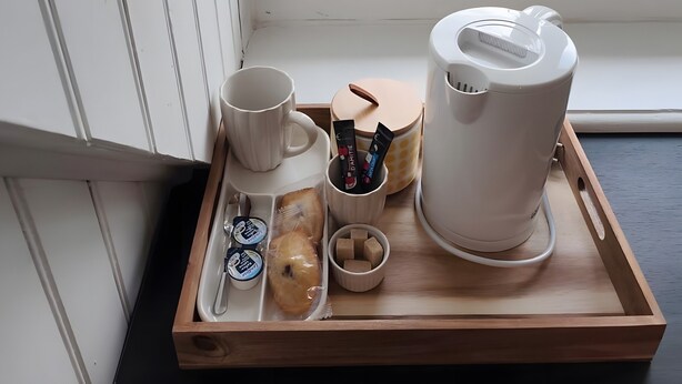 A tray with a coffee maker, mug, and containers of snacks by a window with a view of greenery.