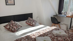A bedroom with a bed, pillows, a desk, and a window.