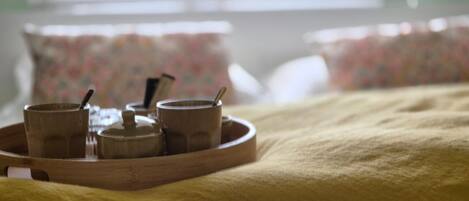 Una cama con un edredón amarillo y una bandeja con tres tazas y una tetera.