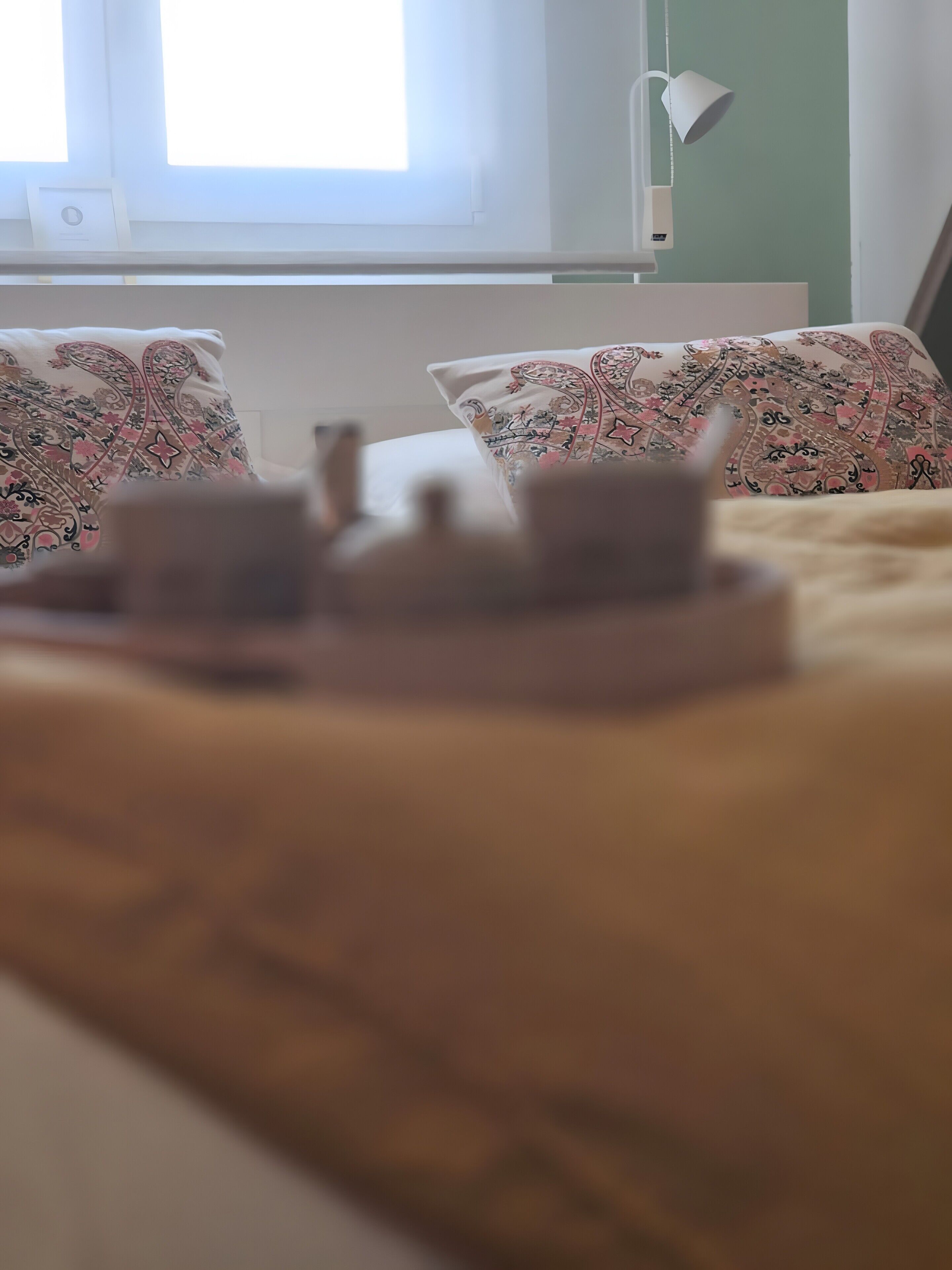 Ein Bett mit gemusterten Kissen, eine Nachttischlampe und ein Fenster mit Jalousien.