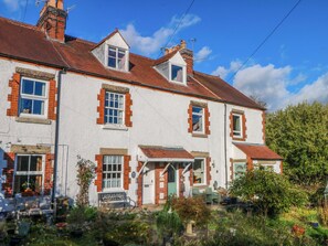A two-story building with a white facade and red brick accents, featuring multiple windows and a small porch area. - Pineapple Cottage (Bakewell)
