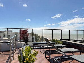 Une terrasse sur le toit, dotée de chaises longues, d’une rambarde et offrant une vue sur l’océan.