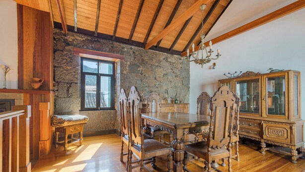Uma sala de jantar com mesa e cadeiras de madeira, parede de pedra e uma janela grande.
