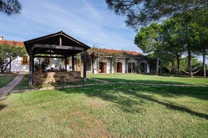 A covered outdoor area with stone walls, a grassy lawn, and a building with a red-tiled roof. - Casa de Campo Vale do Asno-Bungalow '6' with Shared Pool, Wi-Fi and Air Conditioning (Castro Marim)