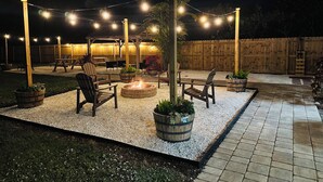 Un espace extérieur aménagé en terrasse, avec des guirlandes lumineuses, des chaises en bois, un foyer et des jardinières.