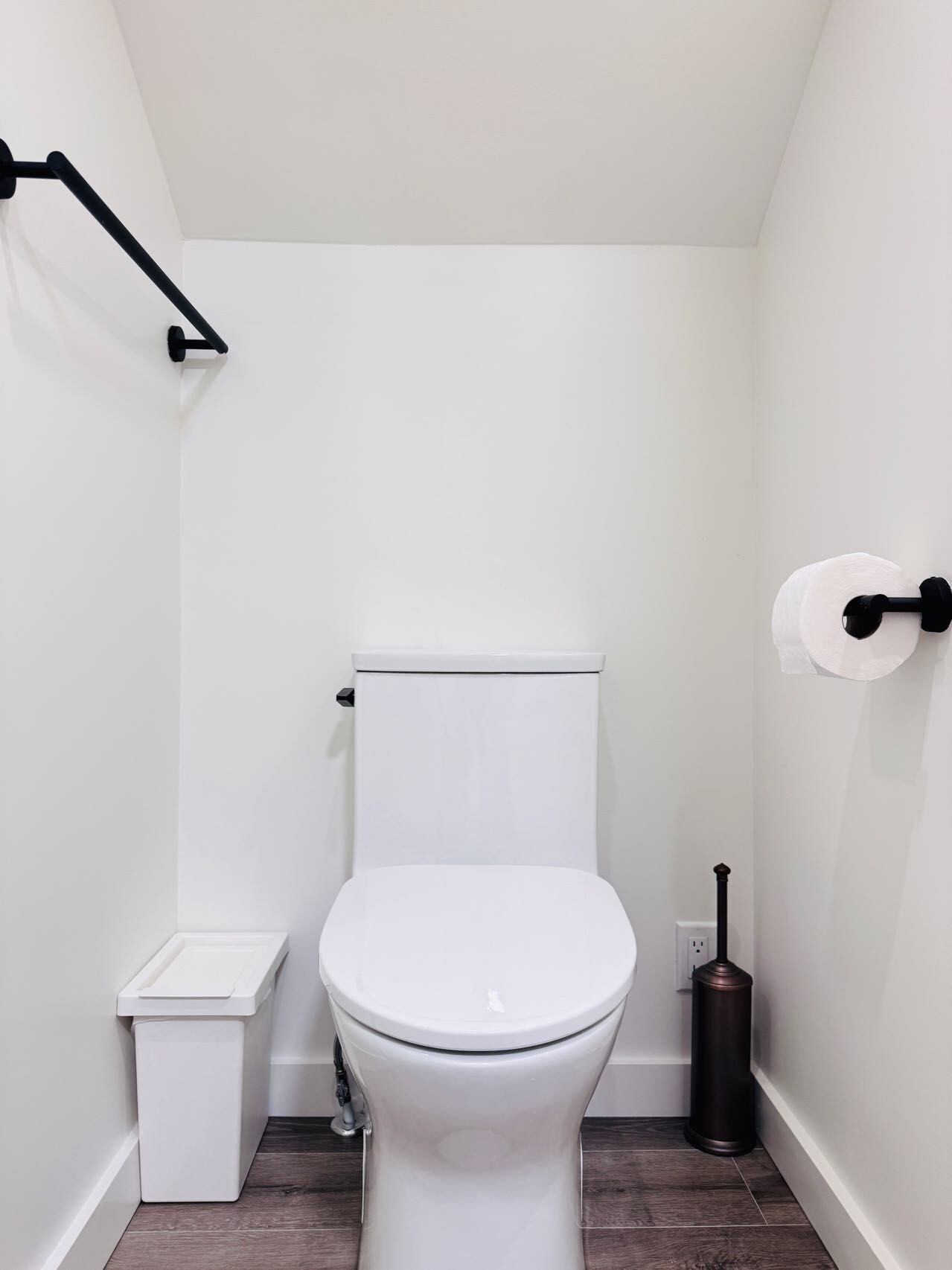 Ein kleines, weißes Badezimmer mit Toilette, Mülleimer und Toilettenpapierhalter.