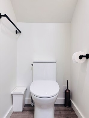 A small, white bathroom with a toilet, a trash bin, and a toilet paper holder. - Deluxe Queen Room with Ensuite Bathroom Vancouver West (Vancouver)