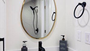 A bathroom with a white sink, a gold-framed mirror, a black faucet, a black soap dispenser, and a bottle of whiskey leather shampoo. - Deluxe Queen Room with Ensuite Bathroom Vancouver West (Vancouver)