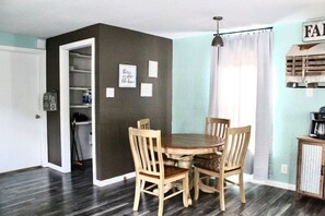A dining area with a round table and four chairs, a kitchen area with a coffee maker, and a door leading to a storage space.