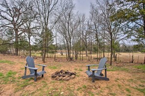 Two Adirondack chairs facing a fire pit in a natural setting with trees in the background.