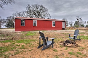 A red cabin with two Adirondack chairs and a fire pit in front.