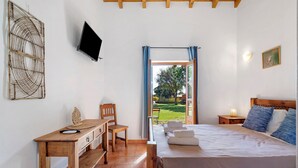 Un dormitorio con cama, escritorio, silla, televisor y ventana con cortinas.