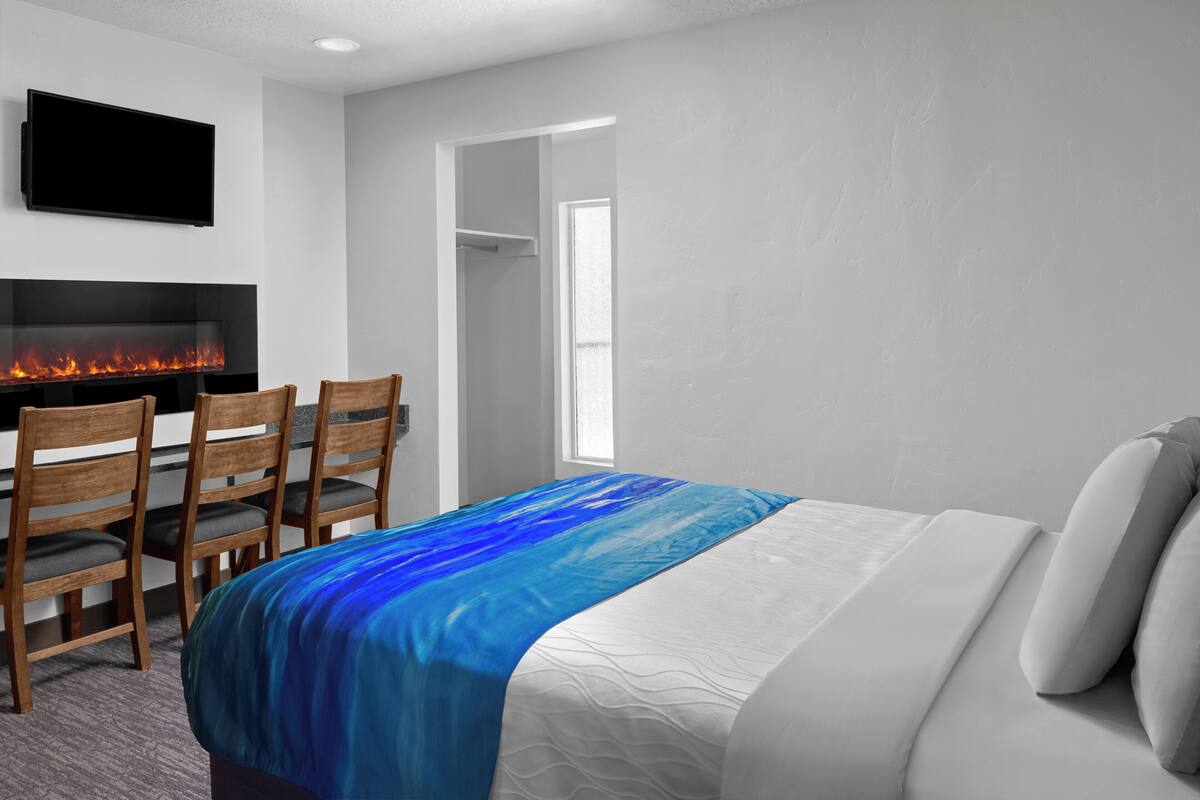Une chambre d’hôtel avec un lit, un téléviseur fixé au mur, une cheminée avec des flammes apparentes et une porte donnant sur une autre pièce.