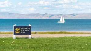 A welcome sign to Blue Water Beach with a sailboat on the water. - Sun Outdoors Garden City Utah (Garden City)