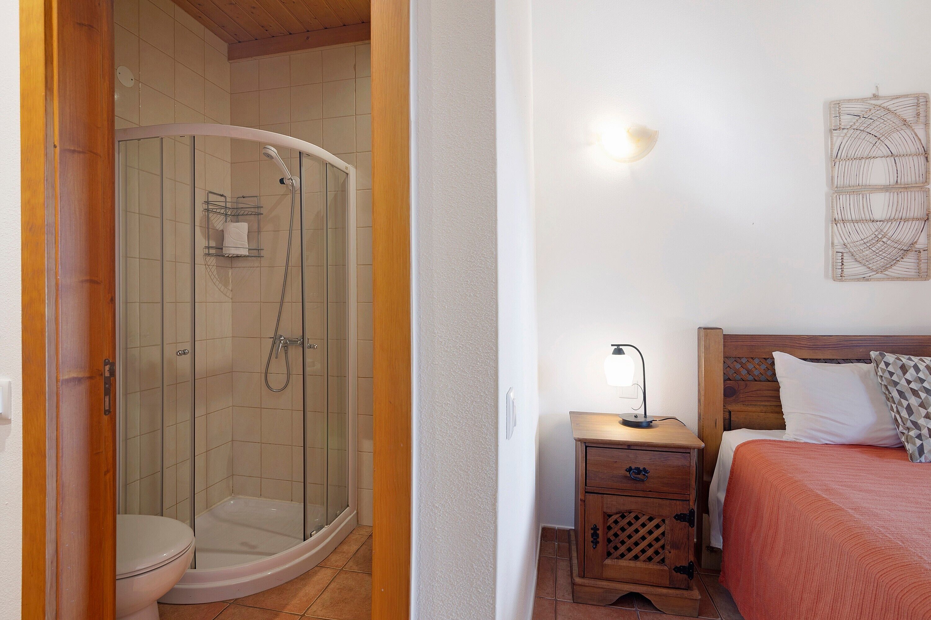 A bathroom with a shower, toilet, and a bedside table with a lamp.