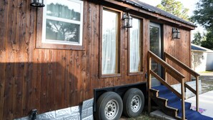 A wooden cabin with a ramp leading to a door, large windows, and a trailer attached with wheels. - Tiny Home Retreat with Bunnies, Chickens & a Goat near Gulf Coast Beach Navarre (Navarre)