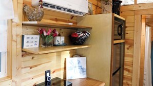 A compact kitchen with wooden walls, a built-in oven, a microwave, and a small countertop with a coffee machine. - Tiny Home Retreat with Bunnies, Chickens & a Goat near Gulf Coast Beach Navarre (Navarre)