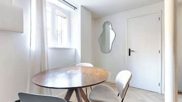 Ein Essbereich mit einem runden Tisch und vier Stühlen, einem Fenster mit Vorhängen, einer Tür und einem Wandspiegel.