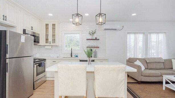 A modern kitchen with white cabinetry, stainless steel appliances, and a central island with two chairs. - Stylish EaDo Apt | Restaurants, Stadiums, Venues (Houston)