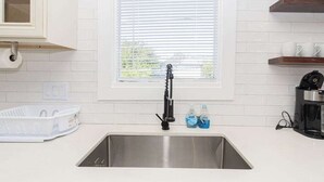 A kitchen with a stainless steel sink, a window with blinds, a dish rack, and a coffee maker. - Stylish EaDo Apt | Restaurants, Stadiums, Venues (Houston)