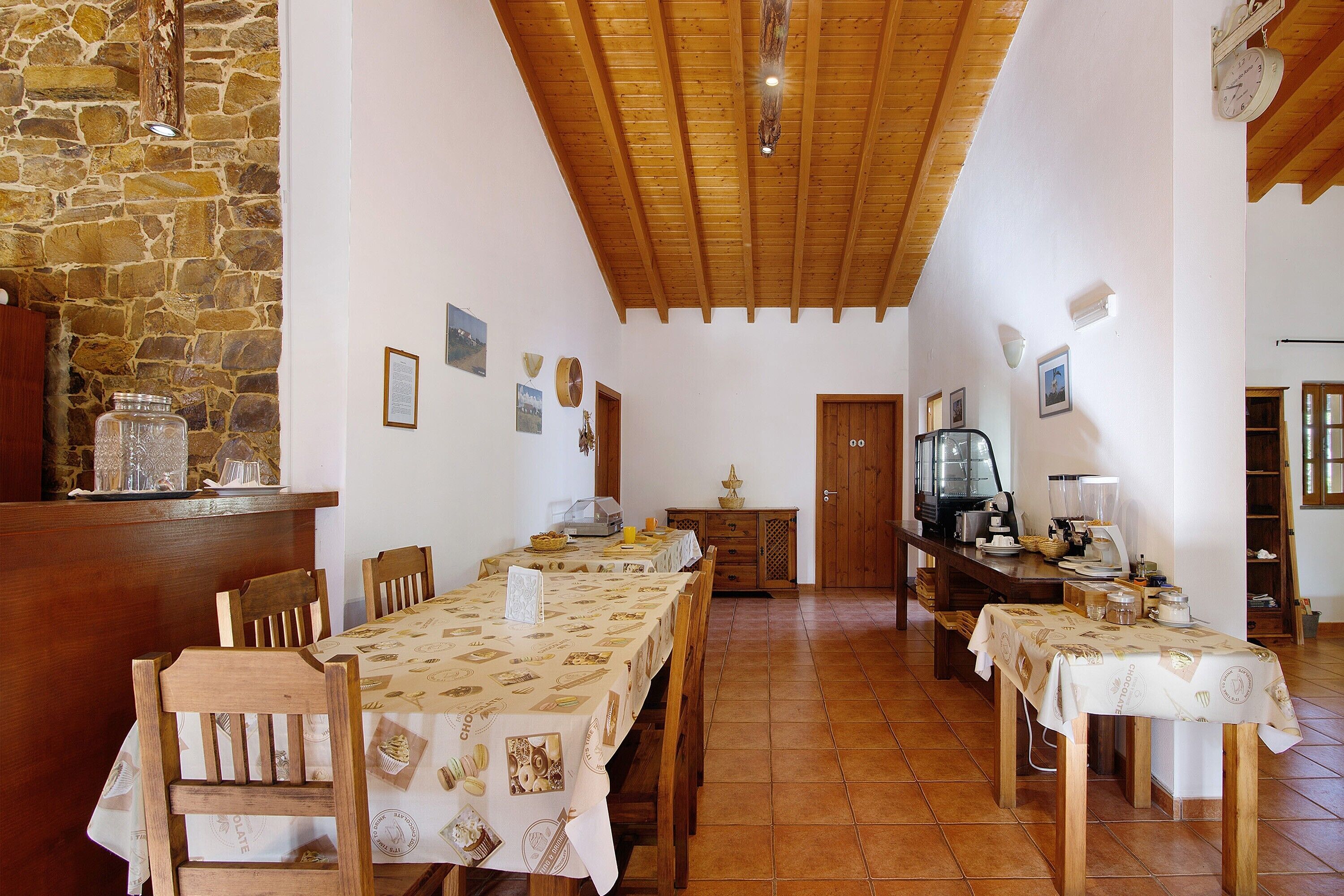 Un espace repas avec des tables et des chaises en bois, un mur en pierre et un plafond en bois.