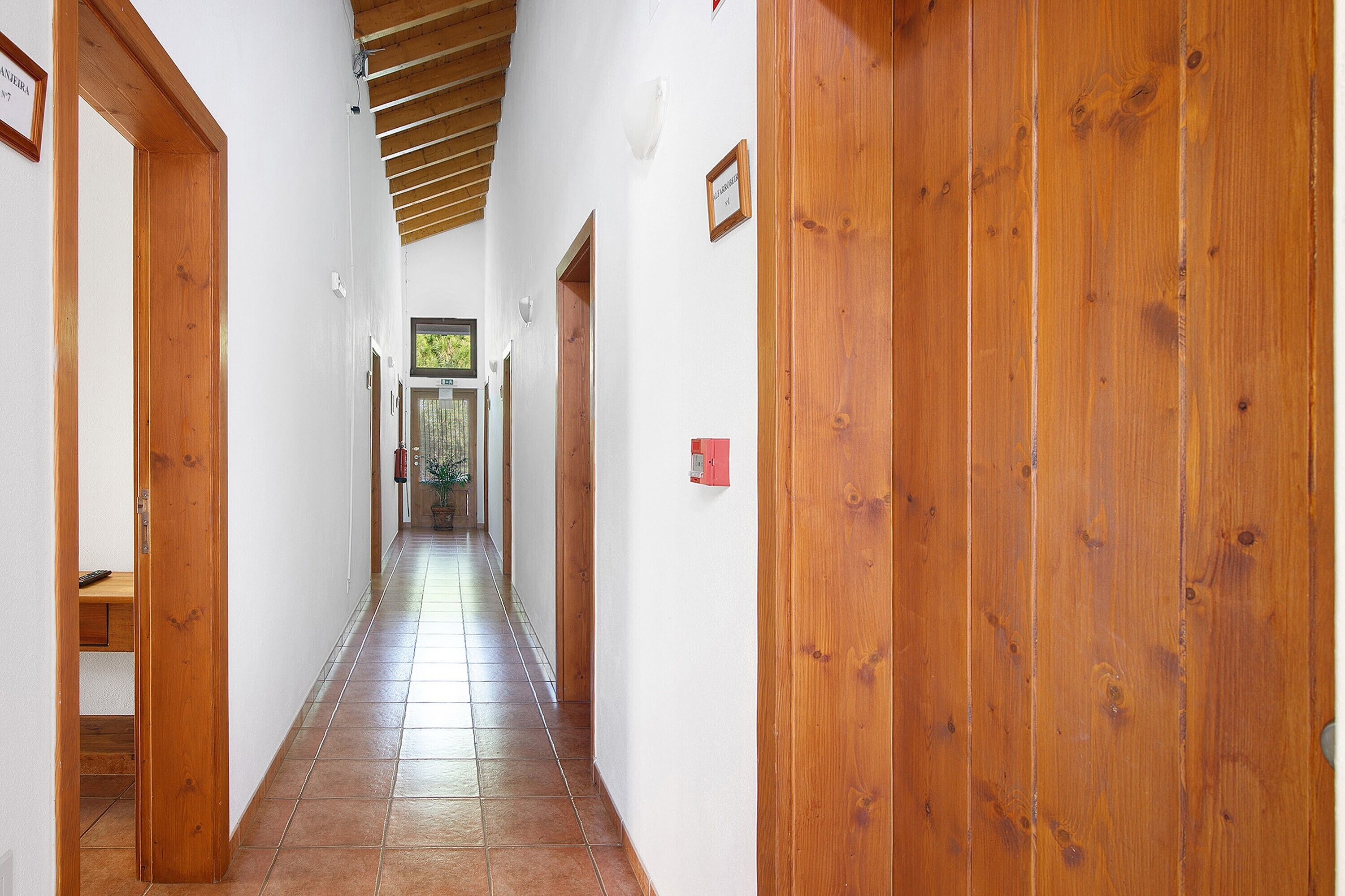 Un pasillo con puertas de madera, paredes blancas y suelo de baldosas.