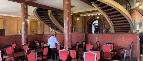 A restaurant with red upholstered chairs, wooden tables, and ornate columns.