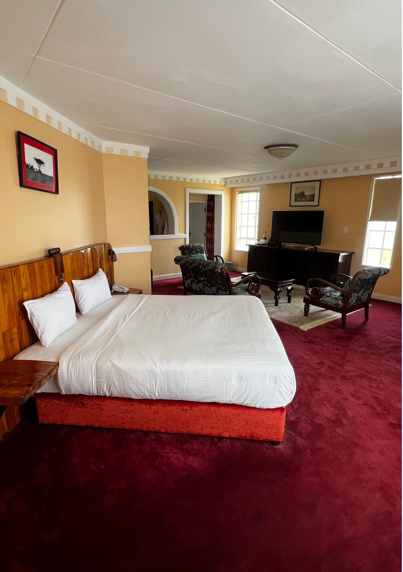 A hotel room with a large bed, two armchairs, a TV, and a desk.