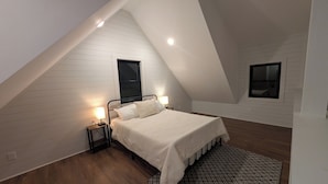 A bedroom with a sloped ceiling, a bed with a white bedspread, two bedside lamps, and a patterned rug.