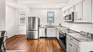 A modern kitchen with white cabinetry, stainless steel appliances, and a wooden floor.