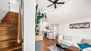 A modern interior with a wooden staircase, white walls, a kitchen area, and a living room with a sofa and coffee table.