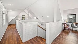 A modern loft with a wooden floor, white walls, and a staircase leading to a lofted area.