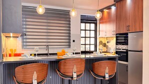 A modern kitchen with a central island, three wooden bar stools, pendant lighting, and stainless steel appliances. - Jacob's Courts Apartment 6 In Kampala (Kampala)