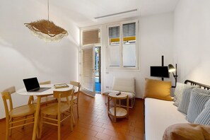 Une pièce de taille modeste comprenant un lit, une petite table avec un ordinateur portable, une chaise, un canapé et un luminaire suspendu.