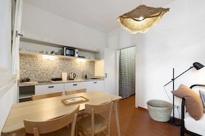 A compact kitchen with a dining area, a woven light fixture, and a patterned curtain.